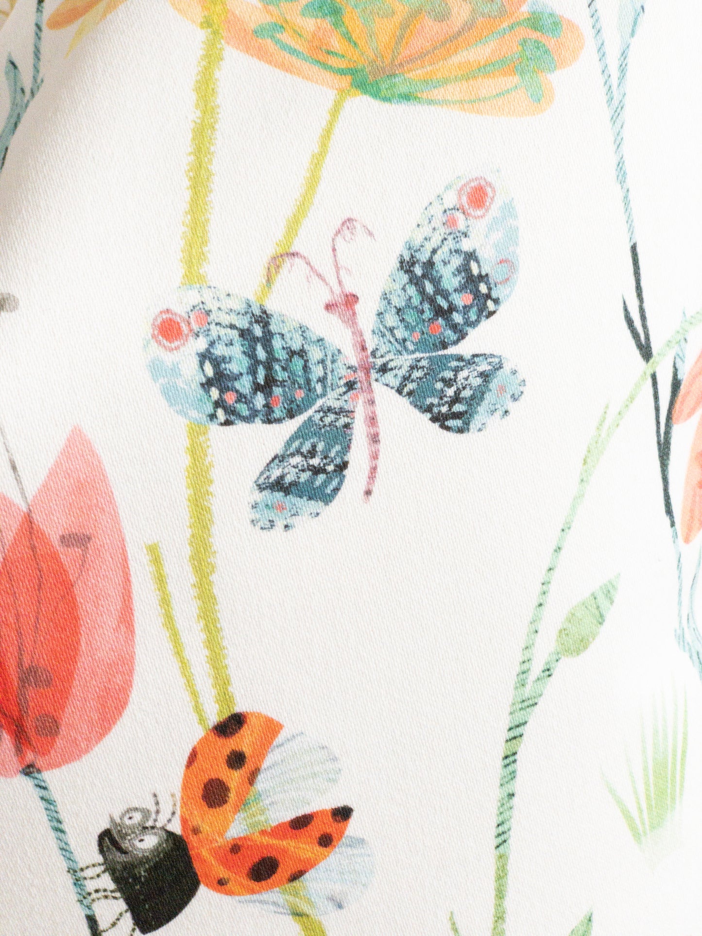 Close up of insect and floral decorative pillow with brightly colored butterflies and ladybugs on a white background.