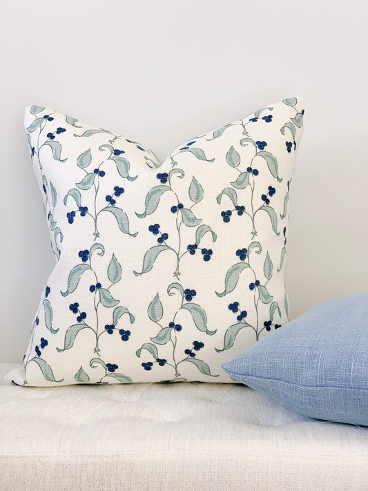 Front view of blue and white decorative pillow with blue and aqua vines on a white linen background.