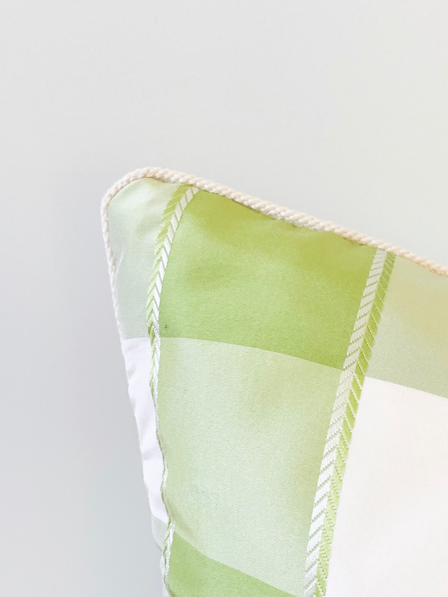 Close up view of green and white plaid pillow with micro trim.