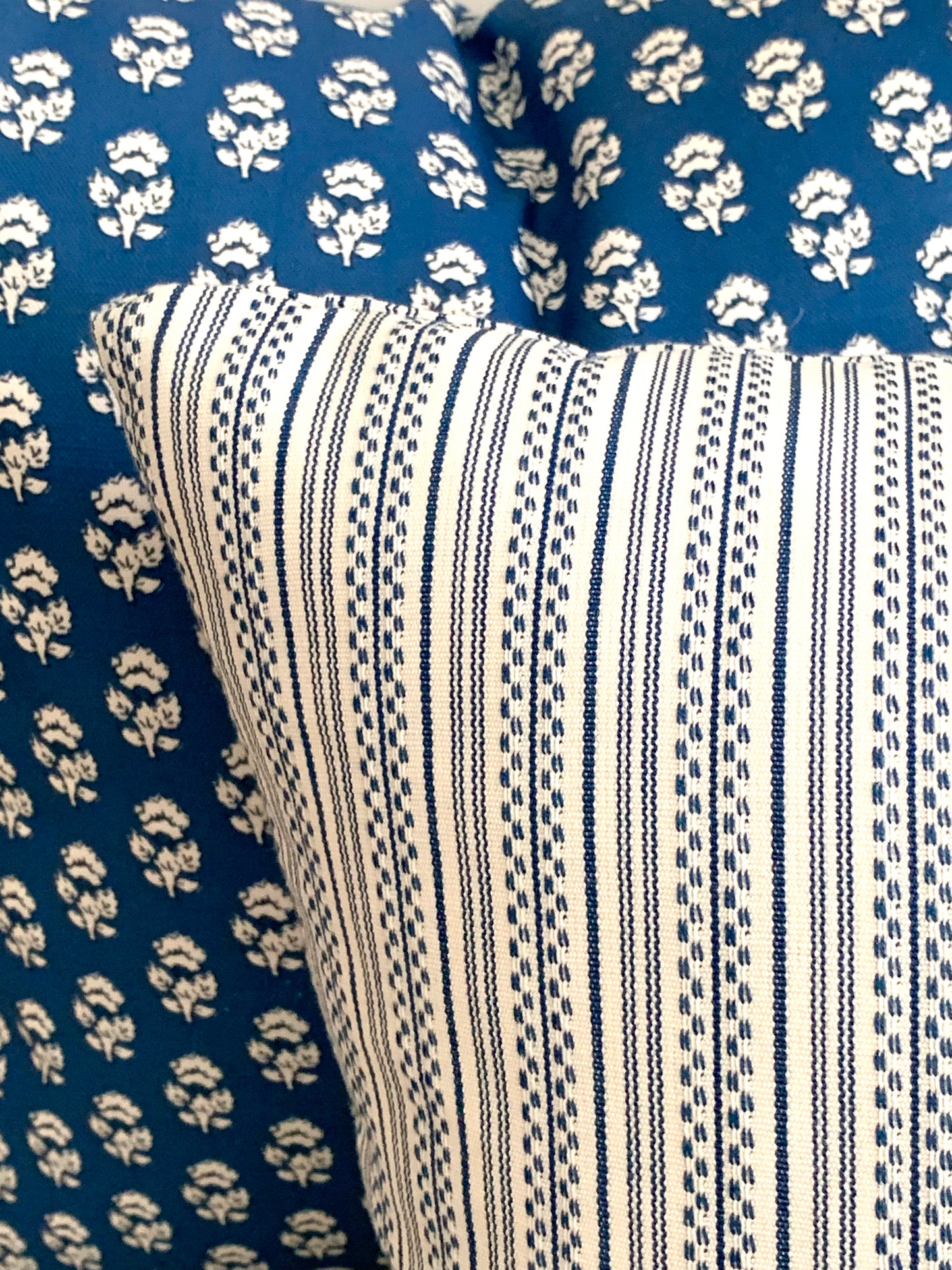 Striped blue and white decorative pillow against a dark blue floral pillow