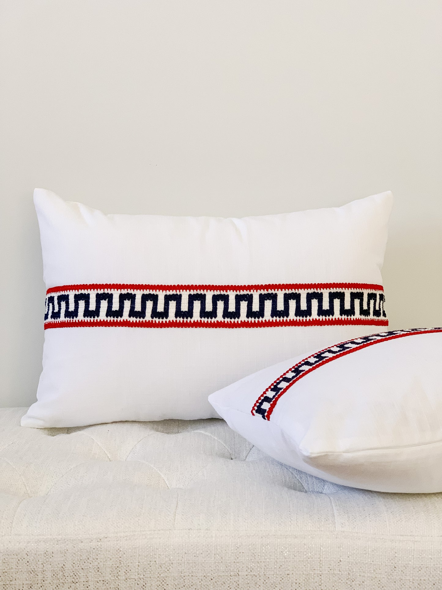 white cotton lumbar designer pillow with red white and blue decorative tape running across middle
