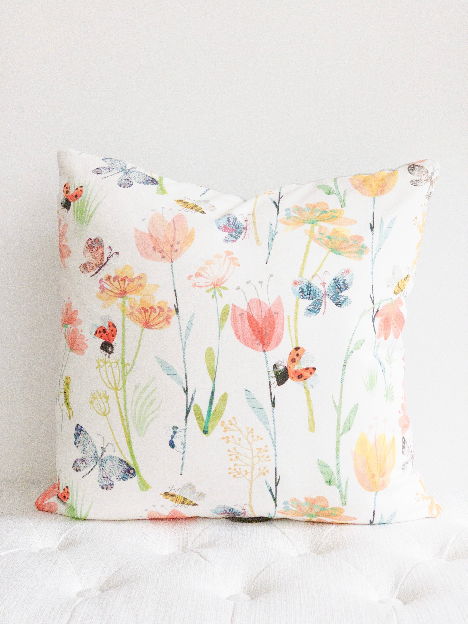 White square decorative pillow with floral and insect motif.  Spring decor floral pillow with white backround.
