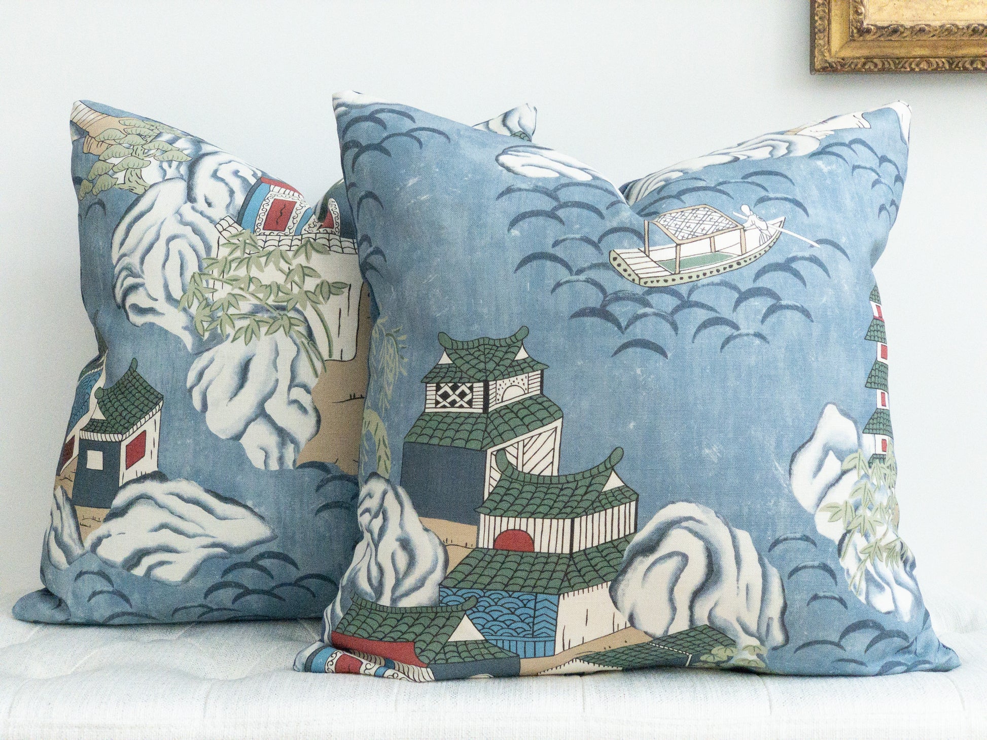 Two square blue decorative pillows with chinoiserie detail of teahouses and boats on water