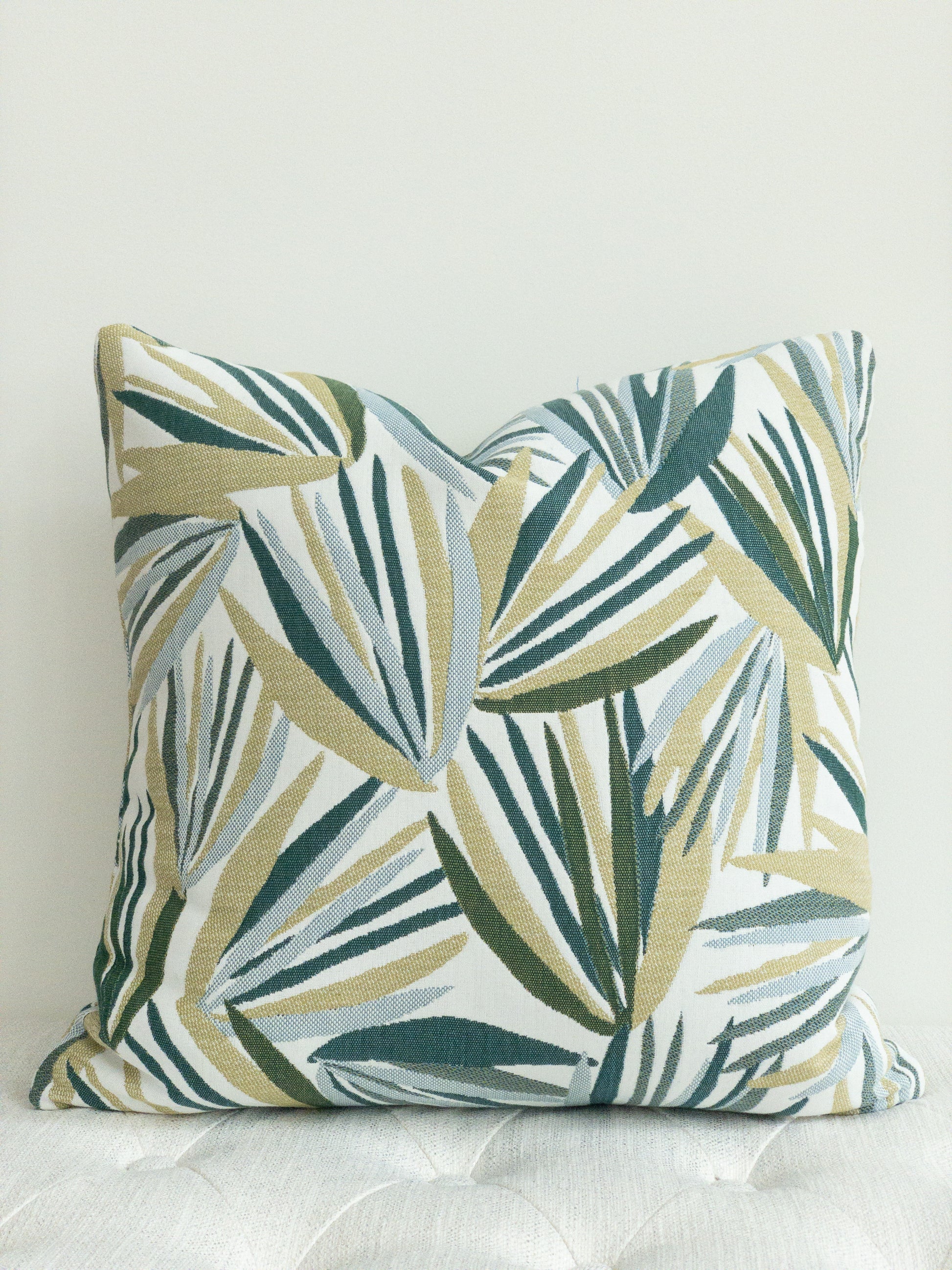 Square designer indoor outdoor pillow with palm motif in shades of green on a white background,