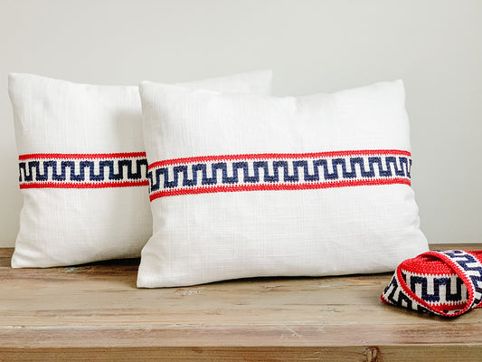 Small white lumbar pillow with red white and blue decorative tape across middle of pillow